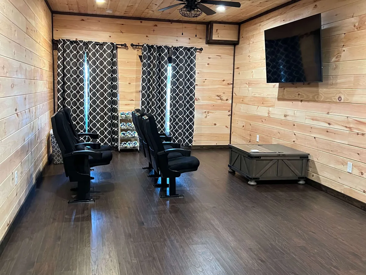 A dedicated theater room with plush reclining chairs is arranged in rows facing a large flat-screen TV. Decorative curtains and warm wooden paneling create an immersive, cozy environment, inviting group movie nights and shared entertainment experiences.
