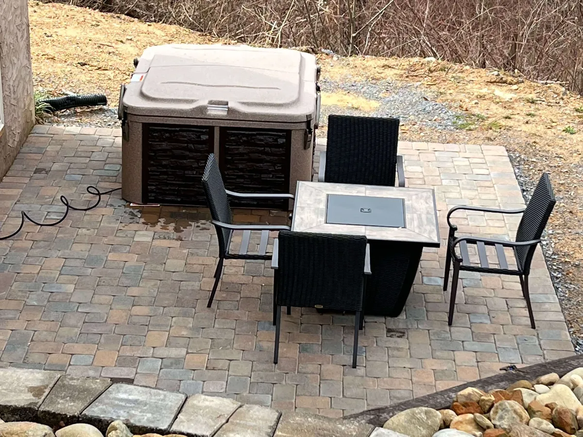 An inviting outdoor space featuring a bubbling hot tub, comfortable seating, and a patio table. The area captures a sense of relaxation and socializing, with the possibility of enjoying sunsets or stargazing while in the hot tub.