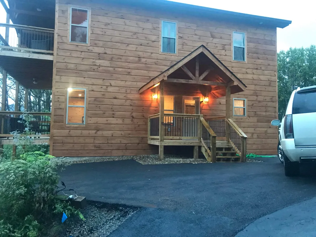 The front porch of a cabin, complete with warm wooden siding and illuminated by entryway lights. The setting invites gatherings, casual conversations, and appreciation of the outdoors, evoking an inviting, cozy mood.