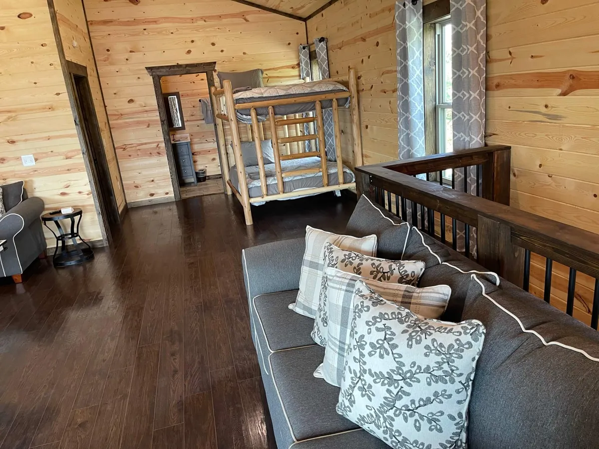A multi-purpose gathering space with a comfy sofa, decorative pillows, and a bunk bed set against classic wooden walls. The room feels informal and family-friendly, perfect for group hangouts, storytelling, and casual fun.